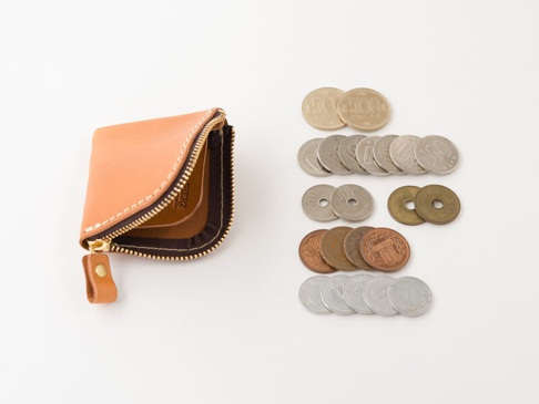 淺棕色皮革製成、拉鍊式開放的職人手作零錢包，內部有分隔設計，旁邊擺放著日圓硬幣。