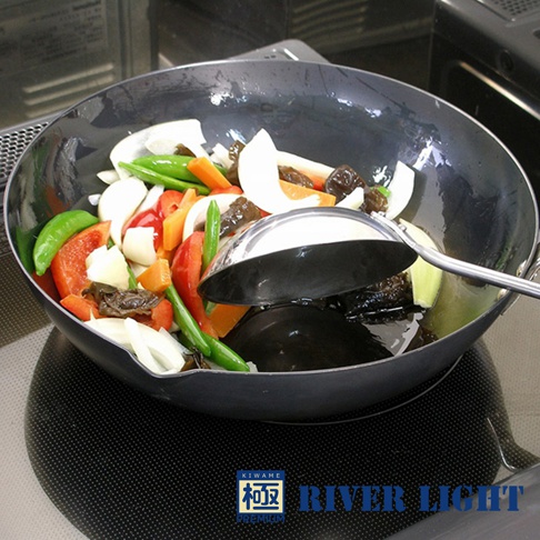 極PREMIUM不易生鏽炒鍋 (30cm)，黑色鐵鍋中盛滿各種新鮮蔬菜，包括紅甜椒、荷蘭豆、紅蘿蔔、洋蔥、香菇等，鍋內有少量烹調用油，一把銀色金屬鍋鏟置於鍋中。