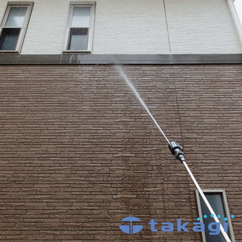 takagi 旋噴頭在清洗棕色磚牆，水柱噴灑在牆面。