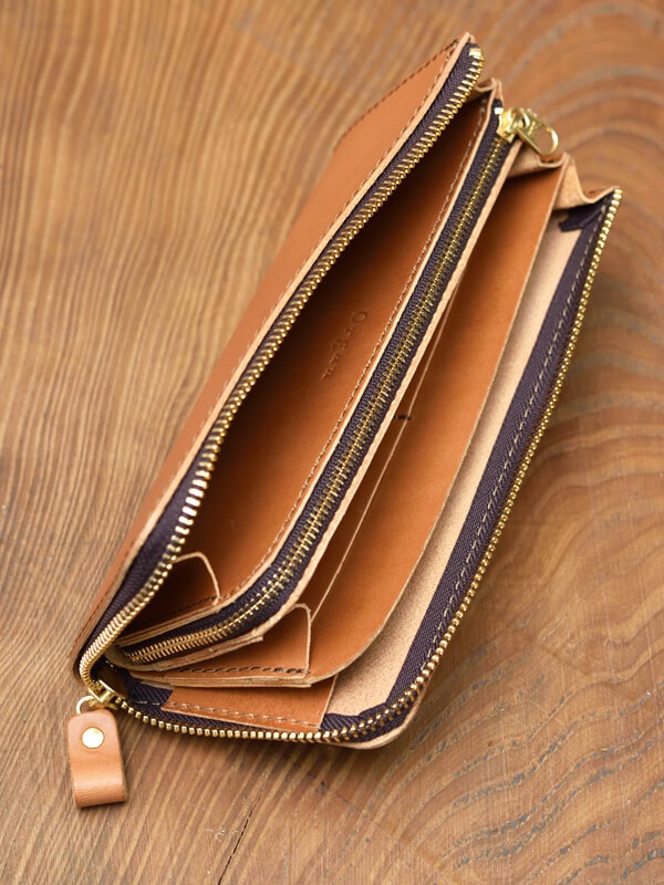 職人手作皮革Organ雙拉鍊L型長夾，呈現自然棕色，雙層結構，內部隔層清晰可見，金色拉鍊，皮革材質，放置於木紋背景上。