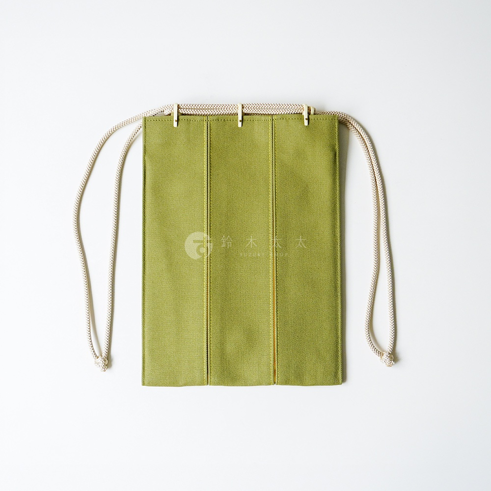 一個極簡風格的綠色帆布信玄袋，正面採用三片式縫製結構，頂部配有米白色繩索提把與金屬固定扣，呈現對稱的長方形設計，整體色調素雅清新，背景為純白色。