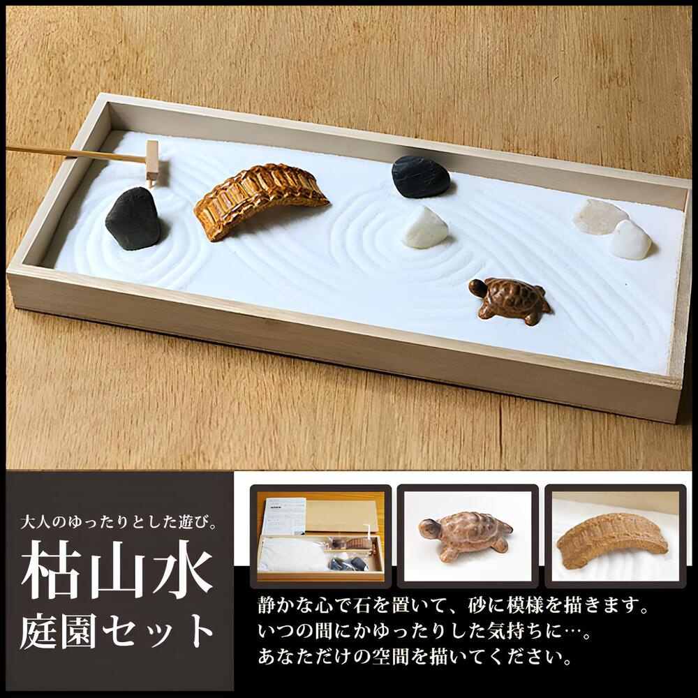 淺色木框枯山水沙盤，內有白色細沙，耙製出水波紋。沙上擺放著黑色、白色鵝卵石，一座棕色仿木質拱橋，一隻棕色陶瓷小烏龜，以及耙沙工具。