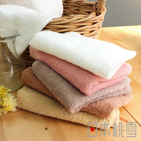 堆疊的飯店方巾，顏色包含白色、粉紅色、褐色、淺棕色和米白色，質地柔軟，部分堆放在藤編籃中，一旁擺放著玻璃瓶和黃色花朵。