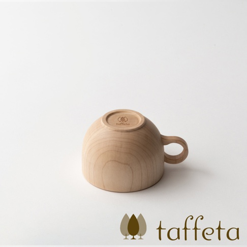 一個由淺色楓木製成的茶杯，杯身圓潤，帶有一個彎曲的把手。杯底朝上，印有品牌標誌和名稱。