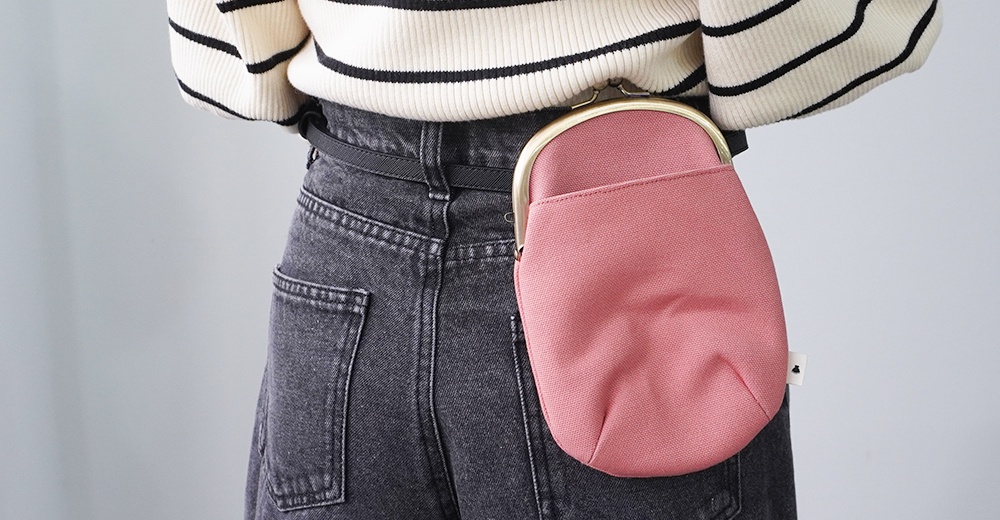 一個斜挎的粉色帆布口金包，掛在身穿條紋毛衣和黑色牛仔褲的腰間