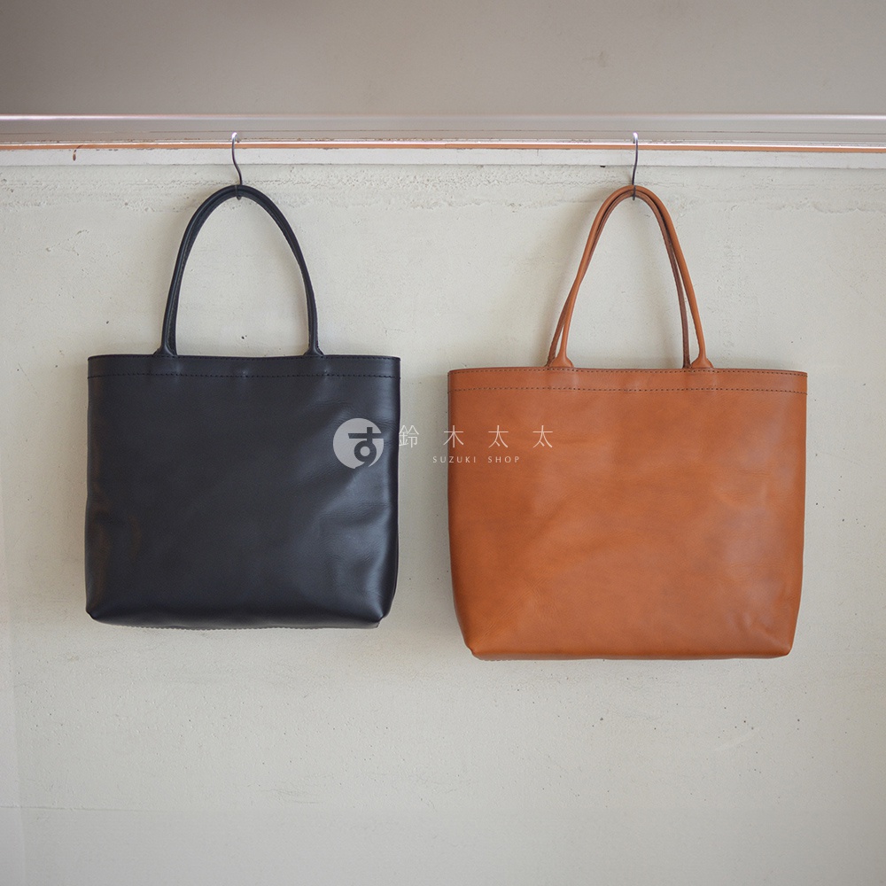 圖片內文字總字數為 12 字。 依據判斷步驟，選擇模式 B。 兩個皮革托特包，一個黑色，一個棕色，皆為簡約方形設計，掛在牆上展示。