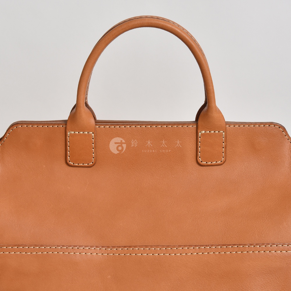 職人手作皮革大容量兩用托特包 T-8，淺棕色皮革，雙提把設計，車縫線精緻，中央有品牌標誌。