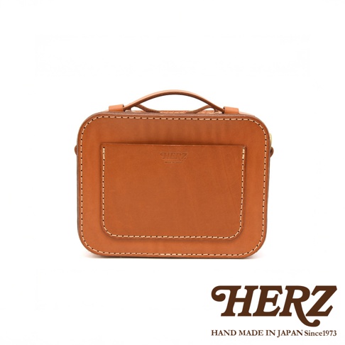 HERZ 職人手作皮革兩用迷你小方包，棕褐色硬皮革材質，正面有壓印品牌標誌與MADE IN JAPAN字樣，車縫線清晰，附手提把，可斜背或側背。