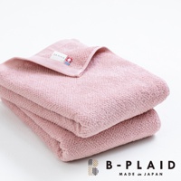 粉紅色今治毛巾，表面有細緻的鱗紋織紋，材質觸感柔軟，疊放整齊，標籤上印有「B-PLAID」字樣及紅藍色標誌。