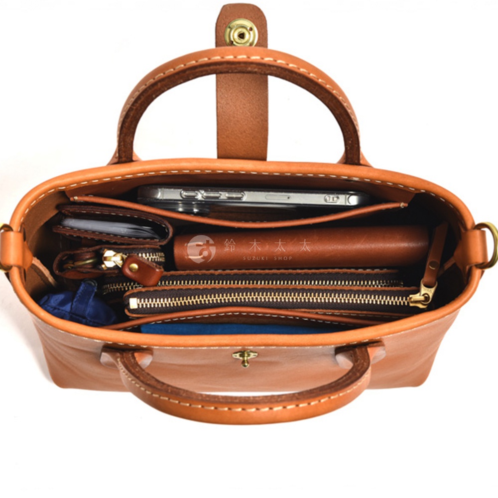 職人手作皮革迷你托特包 T-11，棕色皮革製成，包內展示手機、皮夾、零錢包及其他小物，整體結構清晰，皮革紋理自然，配有金屬拉鍊與旋轉鎖扣。