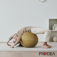 一名兒童正俯臥在一個橄欖綠色的彈力平衡球上，雙手撐地，身體向後彎曲。平衡球由針織材質製成，整體呈圓形，帶有縫線。