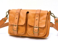 職人手作皮革水洗加工前雙口袋肩背包，呈現自然棕褐色，雙層前袋設計，配有皮革束帶及銅色金屬釦環，質感皮革搭配簡約風格，適合日常攜帶。