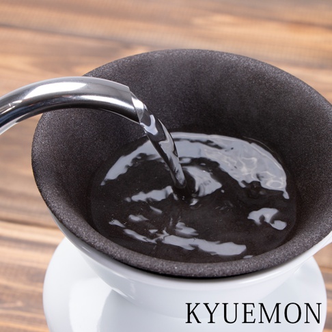 黑色濾杯組，內部有水正在注入，濾杯外層為白色支架，背景為木紋桌面。