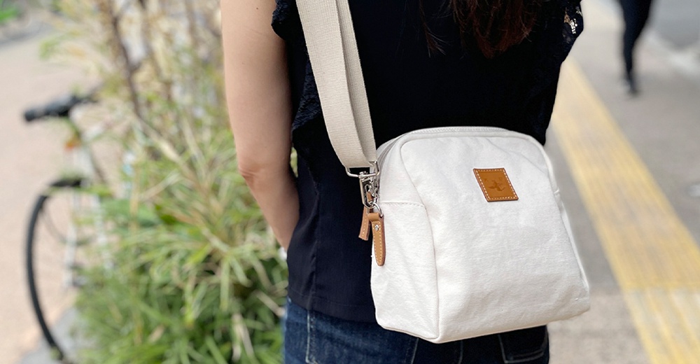 一個身穿黑色上衣和牛仔褲的人，背著一個白色石洗帆布散步包，包上有一個小巧的皮革標籤。