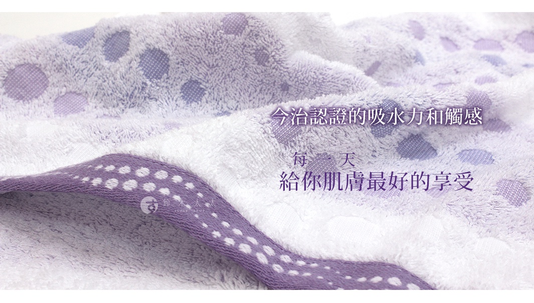 今治水泡泡浴巾，以柔軟的棉質製成，呈現粉紫色和白色交織的細緻紋理，布面上點綴著大小不一的紫色圓點圖案，邊緣滾有紫色的條紋，整體觸感蓬鬆。