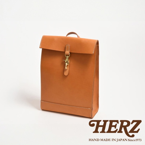 職人手作皮革紙袋風後背包，採用光滑棕色皮革製成，配有黃銅扣環和縫線細節，風格簡約。