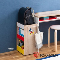 迪士尼系列木質收納櫃，木紋色，附滾輪，側面有米奇圖案，上方放置黑色書包，櫃內有書本、紅色和黃色抽屜，左下角有「©Disney」標誌。