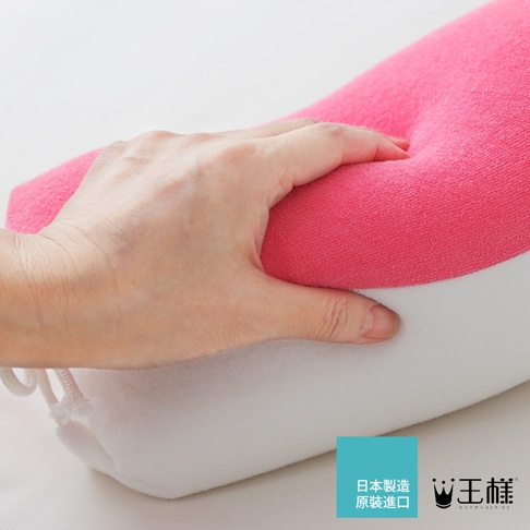 一隻手按壓著粉紅色的圓柱形糖果枕，枕頭上半部是粉紅色絨毛材質，下半部是白色絨毛材質，枕頭兩側有白色繫繩。