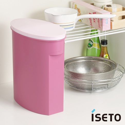 粉紅色塑膠製小家庭儲米桶，附有淺粉紅色蓋子，側面有內凹式把手設計。旁邊架子上擺放著不鏽鋼濾水籃、綠色瓶裝飲料、醬料瓶及其他廚房用品。