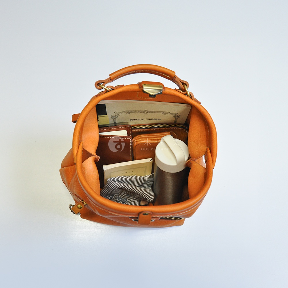 職人手作皮革輕旅行後背包 R-144，橘棕色，展示內部收納，包含筆記本、錢包、水壺及條紋布料，全皮質材質，結構飽滿。