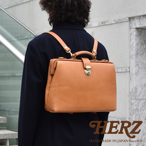 一款棕褐色皮革製的醫生包式三用背包，以單肩或雙肩背帶方式展示，包身有縫線細節與金屬釦環。