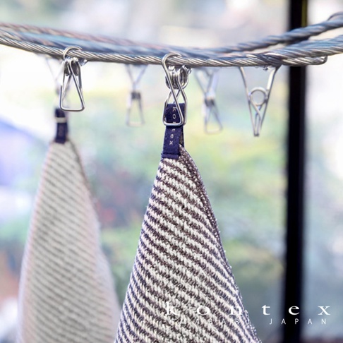 兩條 SWELL 質感波浪鬆餅紋方巾，一條為深棕色與白色條紋，另一條為淺灰色與白色條紋，皆以深藍色織帶掛於金屬曬衣夾上。