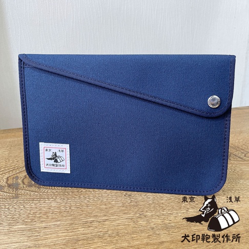 深藍色純棉帆布平板收納包，斜開式翻蓋設計，帶有金屬按扣。包包左下方貼有白色標籤，標示「東京 淺草 犬印製作所」。