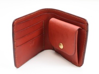 職人手作皮革雙折短夾，經典掀蓋設計，採用紅色皮革製成，內部有多個卡槽及一個帶有金色按鈕的零錢袋。