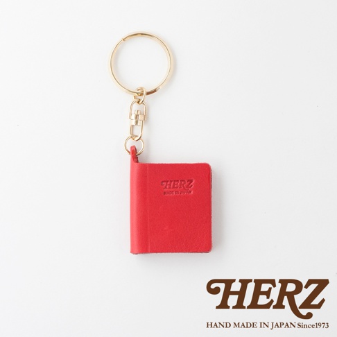 紅色皮革書本造型鑰匙圈，附金色金屬環及鉤扣，書本上壓印有「HERZ」及「MADE IN JAPAN」字樣。