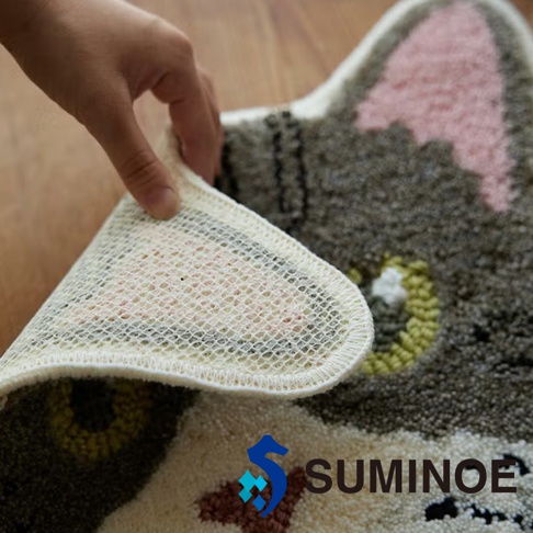 一隻手掀起 SUMINOE NEKOKAO 貓咪造型椅墊的一角，展示其米白色網狀防滑背襯與包邊細節，椅墊正面呈現毛茸茸的貓臉設計，局部可見粉色耳朵與棕色斑紋質感。