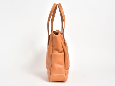 職人手作皮革直式肩背托特包，呈現自然淺棕色，皮革表面帶有細緻紋理，包身側面有一個外插袋，整體以白色背景拍攝。