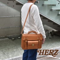 職人手作皮革學院風兩用商務公事包，採用天然皮革製成，呈現溫潤的焦糖棕色。包款設計簡潔，配有手提把、可調式長背帶、雙皮帶釦開合，以及前方小口袋，適合商務或日常使用。