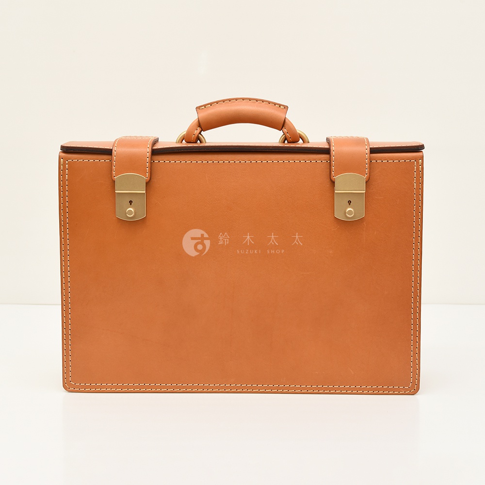 職人手作皮革機師箱，淺棕色皮革，配有金色金屬鎖扣和提把，箱身縫線明顯。