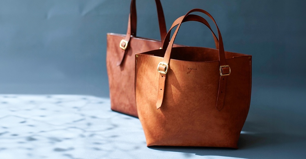北海道KASANE職人手作義大利Margot皮革托特包，雙皮革托特包陳列，近景包上有燙印品牌名稱。