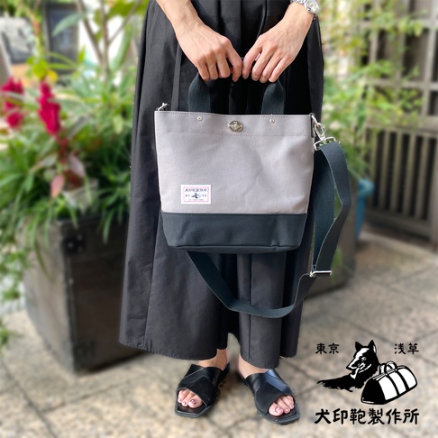 犬印純棉帆布兩用雙色托特包，淺灰色主體搭配黑色底部，設有雙提把及可拆卸斜背帶，包面有品牌標籤。