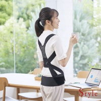 一位女性穿著一件白色短袖上衣，背部佩戴著 BX Pro 美姿調整背帶，這是加強款，尺寸為 S。背帶採用黑色網狀材質和彈性織帶製成，可提供支撐和調整。