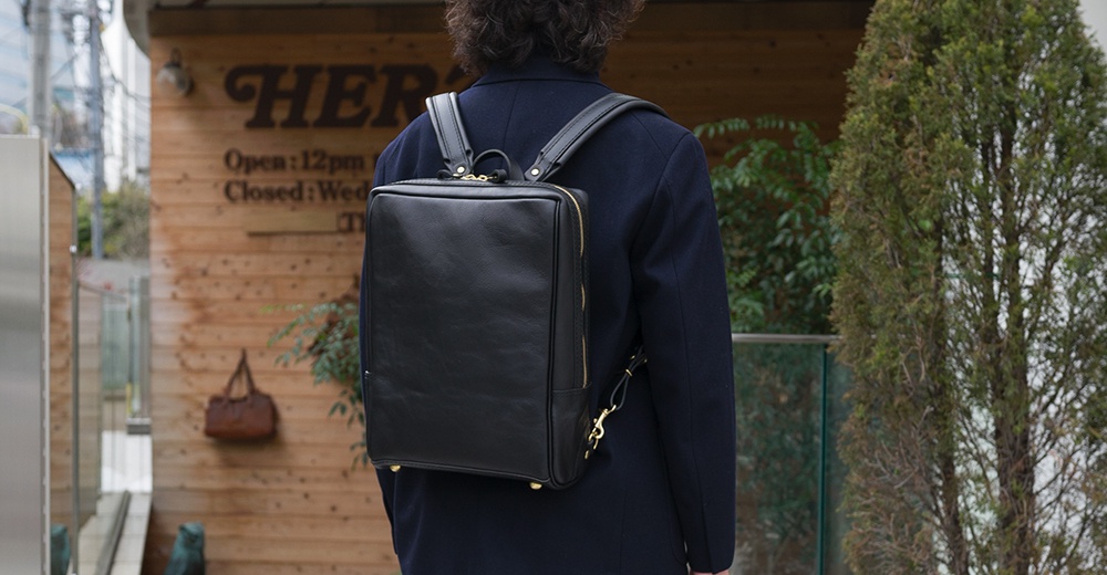 黑色皮革軟皮商務後背包，方形設計，配有金色拉鍊與扣環。