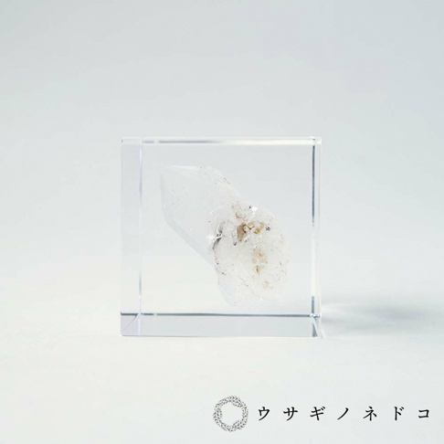 透明壓克力立方塊中封存著一塊天然水晶，水晶呈現半透明的白色，帶有部分雜質和細小的晶體結構。