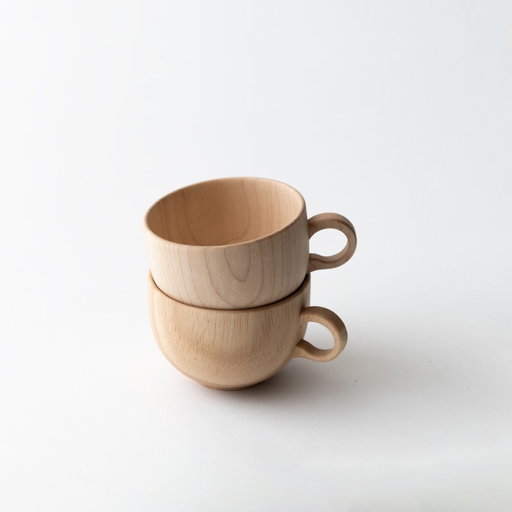兩個淺色楓木茶杯堆疊，帶有圓形把手，呈現自然的木紋。