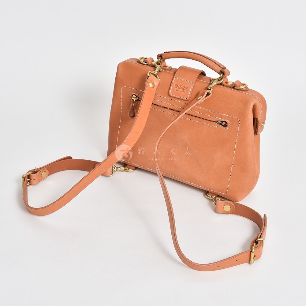 職人手作皮革迷你軟皮杜勒斯包，呈現自然的淺棕色調，質感柔軟，搭配黃銅色金屬扣環和拉鍊，以及可拆卸和調整長度的肩帶。