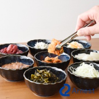 逸品物創不鏽鋼萬用料理夾，銀色，用於夾取泡菜，下方為裝有醃漬物（如醃漬過的梅子、小魚乾、泡菜、醃漬過的白蘿蔔、醃漬過的芥菜等）的深藍色波浪邊小碗。