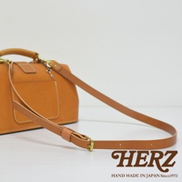 職人手作皮革長型迷你醫生包，採用天然皮革材質，呈現溫潤的焦糖棕色。包款設有手提握把及可調節長度的肩背帶，搭配復古金屬釦件，整體風格簡約而精緻。