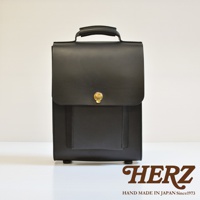 黑色皮革復古後背包，配有頂部提把、正面翻蓋設計及金色鎖扣，包身簡潔，下方有四個圓形腳釘。