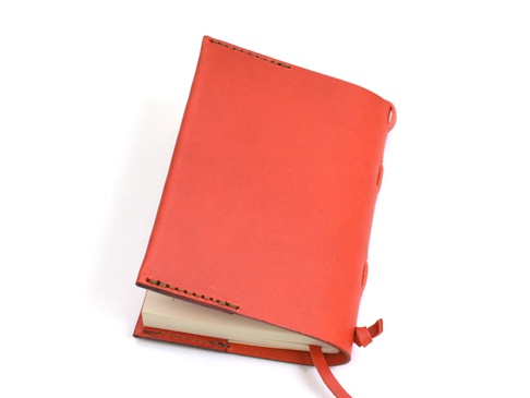 橘紅色皮革書套，側邊有縫線裝飾及綁繩，內含一本白色紙頁的筆記本。