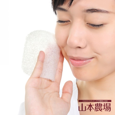 白色蒟蒻QQ薄型海綿，質地輕柔，用於臉部清潔，由手部持有，靠近臉頰。