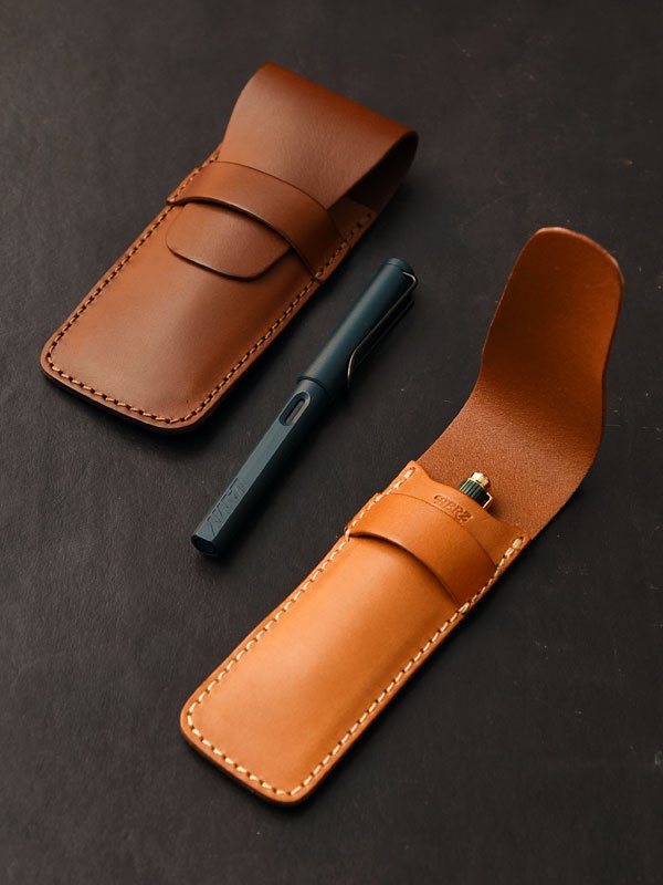兩個焦糖色皮革製的鋼筆收納套，其中一個敞開，內有一支深藍色鋼筆。