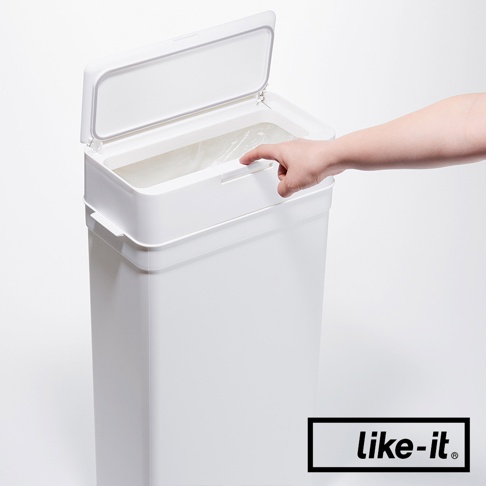 白色塑膠垃圾桶，有按壓式開啟的頂蓋，內置垃圾袋。一隻手正在觸碰垃圾桶前方的按鈕。