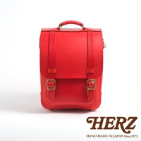 紅色皮革小學生書包，配有兩個黃銅色插扣和提把，手工製作於日本。