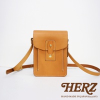 職人手作皮革散步包，淺棕色，方形設計，翻蓋式開口，附有金屬扣。包身有精緻車縫線，搭配可調節長度的皮革背帶。