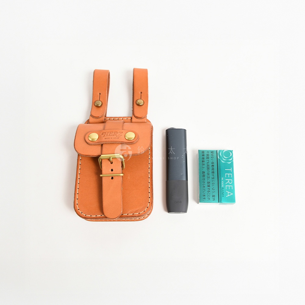 職人手作皮革經典腰袋，淺棕色，帶有金色金屬釦件和縫線。旁邊放置一個深灰色電子煙裝置和一盒綠色香菸。